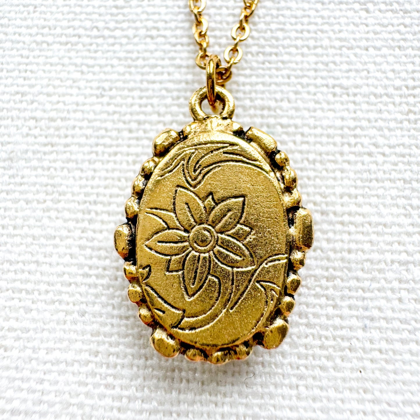 Handcrafted pressed flower pendant necklace set in an ornate vintage gold frame, showing the back of the pendant with embellishments.