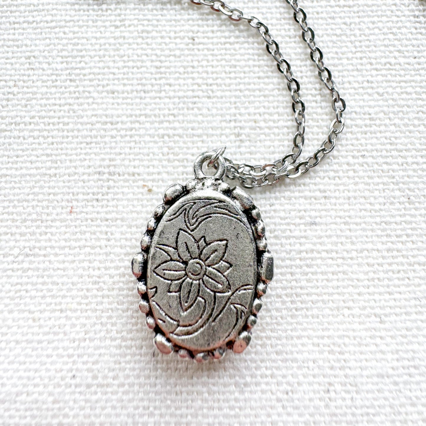 Handcrafted pressed flower pendant necklace set in an ornate vintage silver frame, showing the back of the pendant with embellishments.