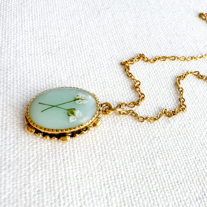 Handcrafted pressed flower pendant necklace featuring real dried Queen Anne's lace flowers against aquamarine backdrop, set in an ornate vintage gold frame, perfect for nature-inspired jewelry lovers.