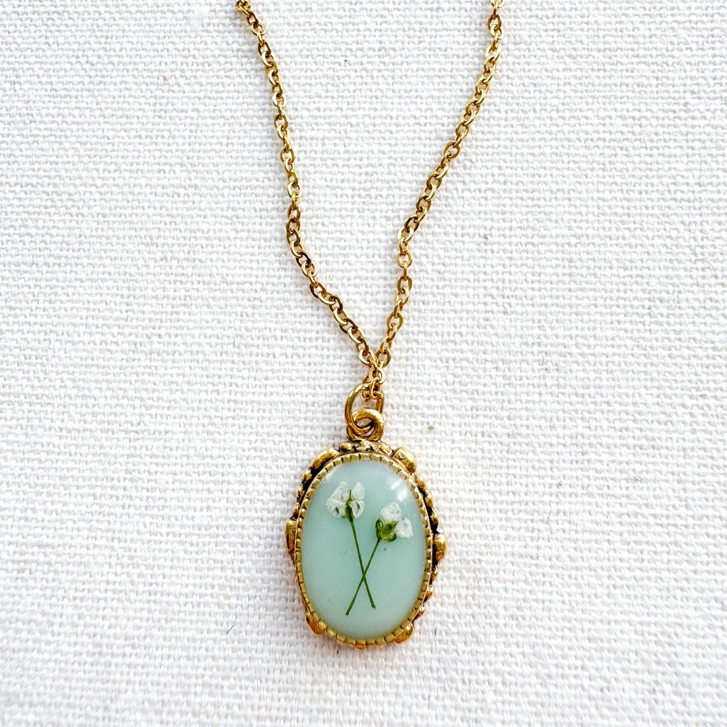 Handcrafted pressed flower pendant necklace featuring real dried Queen Anne's lace flowers against aquamarine backdrop, set in an ornate vintage gold frame, perfect for nature-inspired jewelry lovers.