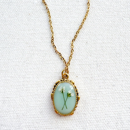 Handcrafted pressed flower pendant necklace featuring real dried Queen Anne's lace flowers against aquamarine backdrop, set in an ornate vintage gold frame, perfect for nature-inspired jewelry lovers.