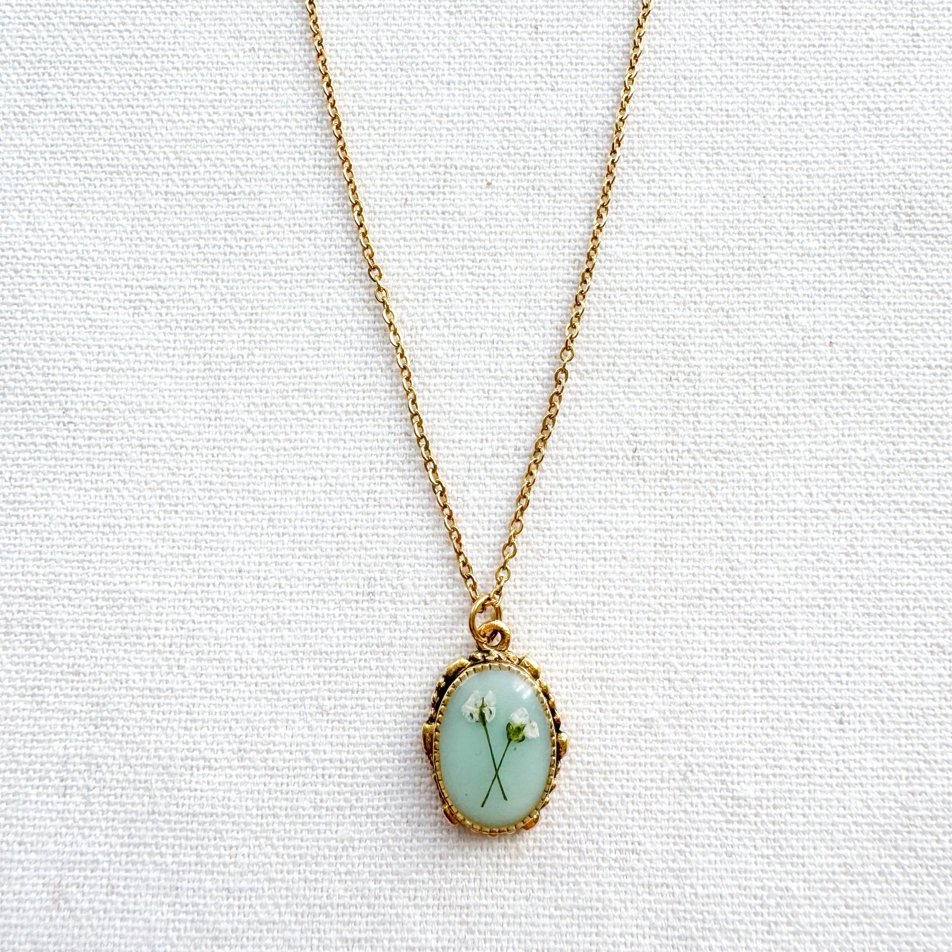 Handcrafted pressed flower pendant necklace featuring real dried Queen Anne's lace flowers against aquamarine backdrop, set in an ornate vintage gold frame, perfect for nature-inspired jewelry lovers.