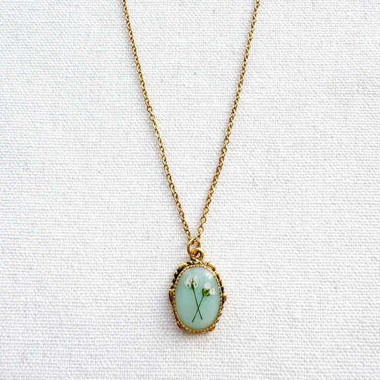 Handcrafted pressed flower pendant necklace featuring real dried Queen Anne's lace flowers against aquamarine backdrop, set in an ornate vintage gold frame, perfect for nature-inspired jewelry lovers.